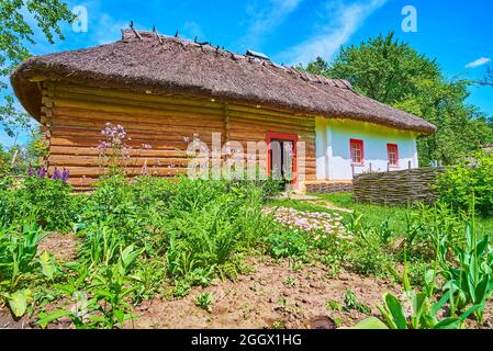 PEREIASLAV, UCRAINA - 22 MAGGIO 2021: Un giardino con fiori alla casa di legno hata con tetto di paglia, Pereiaslav Scansen, il 22 maggio a Pereiaslav Foto Stock