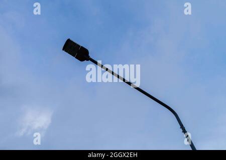 una lampada per l'illuminazione stradale su un palo contro lo sfondo blu della nuvola di cielo Foto Stock