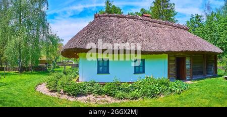 Panorama della casa medievale hata con tetto di paglia e il giardino con prato verde intorno, Pereiaslav Scansen, Ucraina Foto Stock