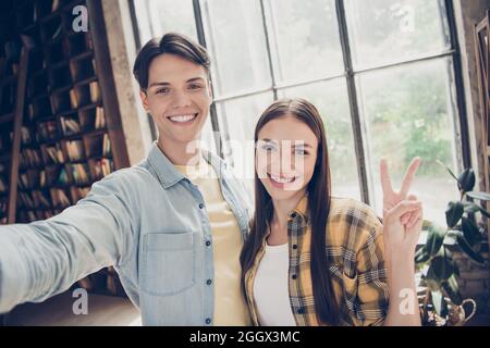 Autoritratto di due attraenti e allegre persone che visitano la biblioteca mostrando V-segno al loft interno industriale spazi aperti Foto Stock