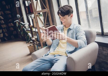 Ritratto di attraente allegro messo a fuoco ragazzo lettura interessante libro al loft interno industriale Foto Stock