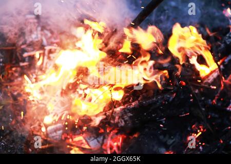 Scintille calde rosse che bruciano volano dal fuoco grande. Carboni brucianti, particelle che fiammano che volano su sfondo nero. Foto Stock