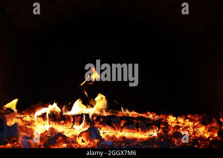 Scintille calde rosse che bruciano volano dal fuoco grande. Bel sfondo astratto sul tema del fuoco. Carboni brucianti, particelle infiammate che volano contro la colpa Foto Stock