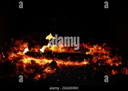 Scintille calde rosse che bruciano volano dal fuoco grande. Bel sfondo astratto sul tema del fuoco. Carboni brucianti, particelle infiammate che volano contro la colpa Foto Stock