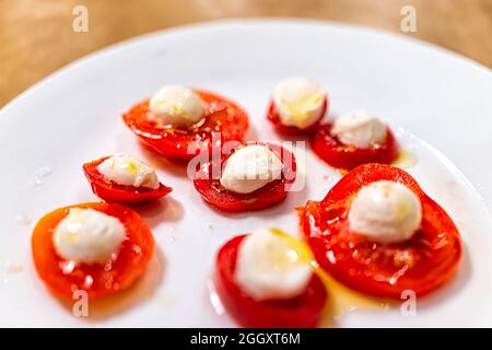 Primo piano di piatto bianco con piccoli pomodori freschi a fette, mozzarella di formaggio cosparsa di olio d'oliva come spuntino o antipasto come capro di ispirazione italiana Foto Stock