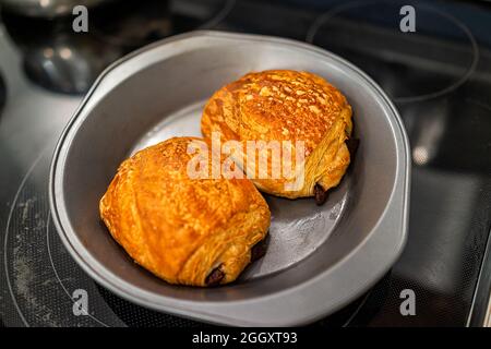 Primo piano di due croissant di pasticceria dorati e bruno sulla teglia da forno con crosta fiocchi e ripieno di cioccolato Foto Stock