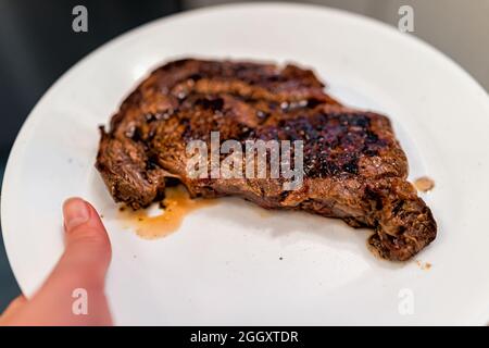 Donna mano che tiene medio raro grigliato erba-alimentato ribeye costola occhio carne di manzo bistecca su piatto bianco che serve Foto Stock