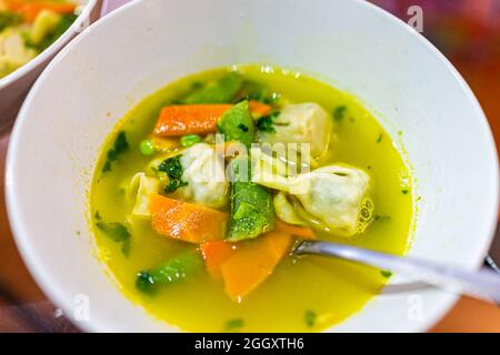 Primo piano della tradizionale ciotola cinese per zuppa wonton con carote e piselli a scatto come pasto asiatico con cucchiaio Foto Stock