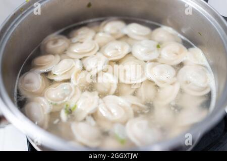 Primo piano macro di acciaio inossidabile pentola su piano di stufa con gnocchi tradizionali russi pelmeni con cottura a vapore di carne bollente Foto Stock