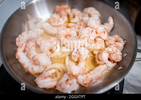 Macrofumo di padella in acciaio inox con olio d'oliva saltato, fette di cipolla dolce e un grande jumbo re intero gamberi argentini frutti di mare cotti o Foto Stock