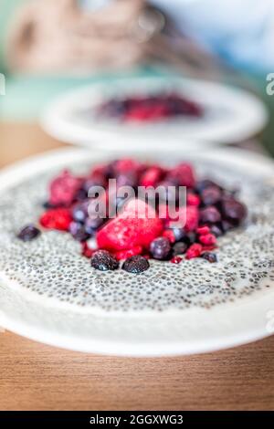 Macro closeup vista laterale di fragole fresche crude, mirtilli e lamponi in semi di chia budino di porridge con latte di mandorla di capra vegana con cucchiaio Foto Stock