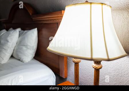Camera da letto serale con scrivania illuminata lampada da notte, cuscini bianchi con lenzuola sulla testiera del letto con materasso Foto Stock