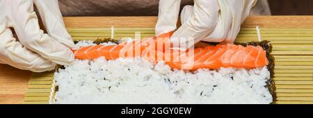 Processo di preparazione del sushi. Le mani da donna in guanti di gomma avvolgono rotoli per sushi e sushi a casa Foto Stock