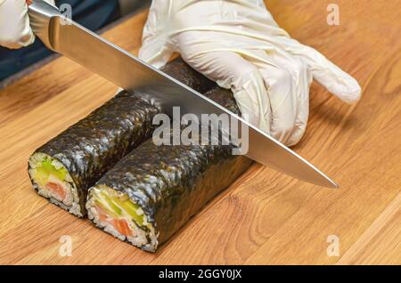 Il processo di preparazione del sushi giapponese. Coltello in mano taglia un primo piano su un asse di legno. Foto Stock