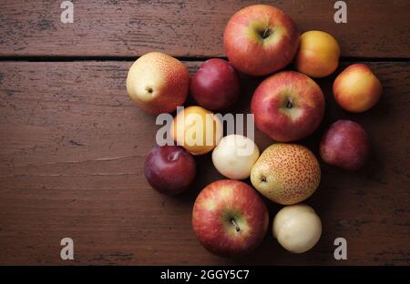 Frutta succosa su un vecchio tavolo di legno. Mele, pere, prugne, albicocche su sfondo rosso scuro. Vista dall'alto Foto Stock
