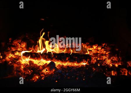 Scintille calde rosse che bruciano volano dal fuoco grande. Bel sfondo astratto sul tema del fuoco. Carboni brucianti, particelle infiammate che volano contro la colpa Foto Stock