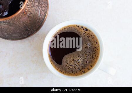 Una tazza e un Turk con caffè appena fatto su una superficie leggera del tavolo, vista dall'alto. Risveglio mattutino, inizio di una nuova giornata. dri energizzante Foto Stock