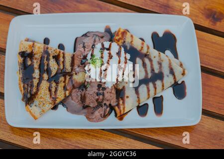 Piatto di confezioni con un cucchiaio di gelato alla vaniglia decorato con crema di cioccolato Foto Stock