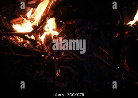 Scintille calde rosse che bruciano volano dal fuoco grande. Carboni brucianti, particelle che fiammano che volano su sfondo nero. Foto Stock