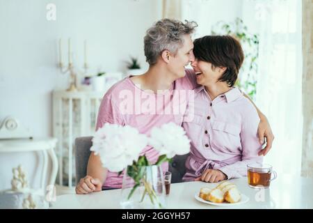 Coppia ridente innamorata di divertirsi durante la colazione in cucina a casa. Abbracci e baci. Momenti felici. Tempo per la famiglia. Messa a fuoco selettiva. Foto Stock