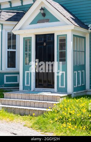 L'esterno di un edificio in legno verde teale di stile coloniale vintage con finiture decorative bianche. C'è una vecchia porta in legno nero con maniglie in ottone. Foto Stock