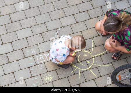 Vista ravvicinata dall'alto verso il basso sul bambino che attingeva su lastre di pavimentazione e sulla donna che lo guardava. Foto Stock