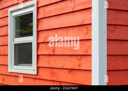 L'esterno di una parete orizzontale in legno stretto rosso brillante di una casa con una finestra in vinile. Il rivestimento sui vetri è bianco. l'outsi Foto Stock