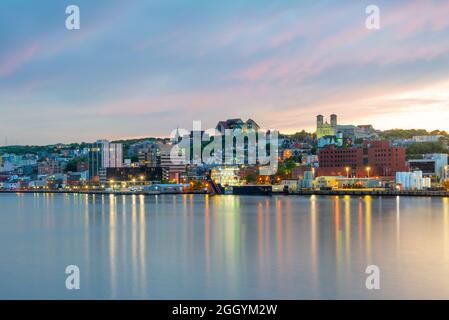 St. John's, Terranova, porto sul lungomare al tramonto. Le luci sull'acqua sono gialle e arancioni che si riflettono dallo skyline. Foto Stock