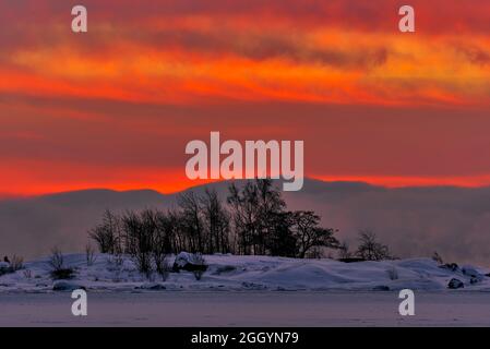 Scena drammatica, tra cui l'alba ardente nella mattinata invernale estremamente fredda con nebbia marina e ghiaccio che copre il Mar Baltico dietro ghiaccio e neve isola coperta AN Foto Stock