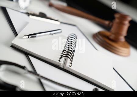 Concetto di legge medica. Gavel, taccuino e stetoscopio sul tavolo di vetro. Luce blu. Foto Stock