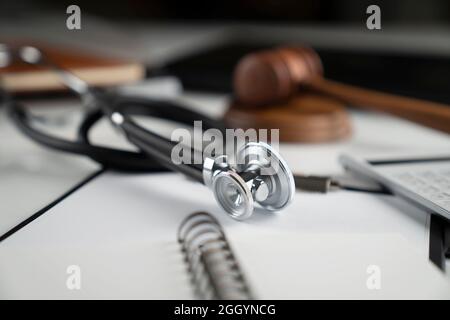 Concetto di legge medica. Gavel, taccuino e stetoscopio sul tavolo di vetro. Luce blu. Foto Stock