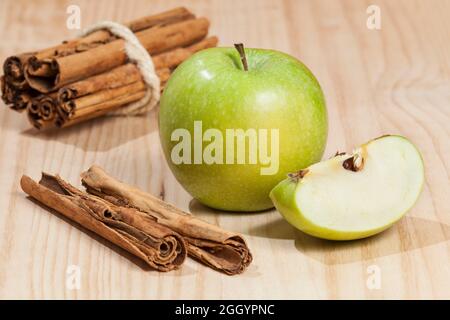 Mela verde con un bastone di cannella; foto su sfondo di legno. Foto Stock