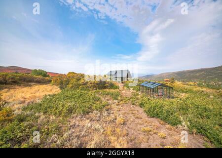 Grande casa a due piani con serra di vetro nel mezzo di un vasto arbusti e erba Foto Stock