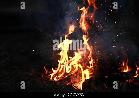 Scintille calde rosse che bruciano volano dal fuoco grande. Carboni brucianti, particelle che fiammano che volano su sfondo nero. Foto Stock