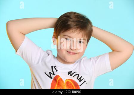 Nel ritratto, un bel ragazzo, sviluppato, intelligente adolescente in una colorata T-shirt ha messo le mani dietro la testa e sorride leggermente, guardando occhio t Foto Stock