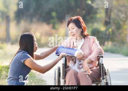 Donna asiatica che prende la loro madre anziana disable per una camminata al parco, Tailandia Foto Stock