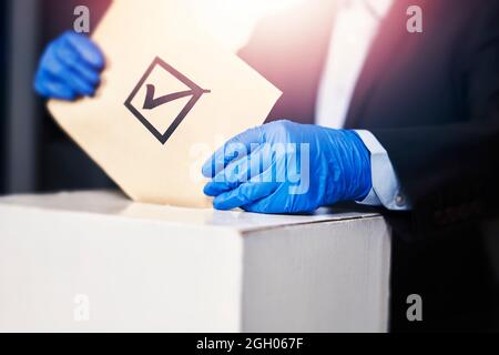 Una persona in guanti medici che votano. Concetto di elezione. Elezioni presidenziali o parlamentari. Un elettore che mette un voto elettorale nella scatola. Elezione Foto Stock