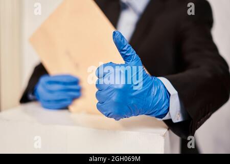 Una persona in guanti medici che votano. Concetto di elezione. Elezioni presidenziali o parlamentari. Un elettore che mette un voto elettorale nella scatola. Elezione Foto Stock