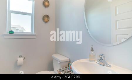 Pano interno di un bagno bianco con finestre, specchio, lavandino e armadio Foto Stock
