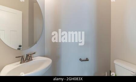 Pano interno di un piccolo bagno bianco con lavandino e specchio Foto Stock