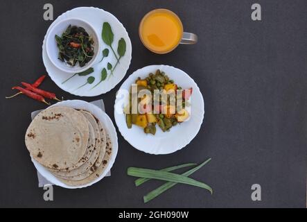 Piatto di paneer matar mix Veg, saag (verdi) e chapati (pane indiano) su piatti bianchi e succo su vetro su sfondo nero con spazio copia Foto Stock