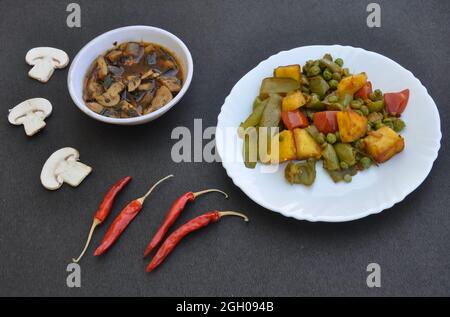 Piatto di veg paneer matar e zuppa di funghi con peperoncini rossi su sfondo nero. Foto Stock