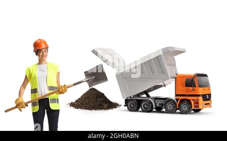 Lavoratore di costruzione femminile con un gilet e un hardhat che tiene una pala di fronte a un camion di scarico isolato su sfondo bianco Foto Stock