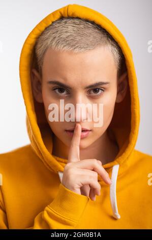 Giovane donna in ocra cappuccio copre il suo volto con mano su sfondo bianco. Foto Stock