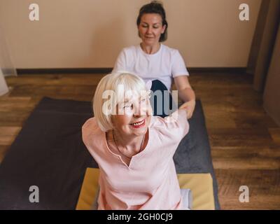 anziana (vecchia) caucasica elegante donna con capelli grigi e phalaenopsis rosa nei suoi capelli seduti al massaggio tailandese. Anti età, stile di vita sano, viaggi Foto Stock