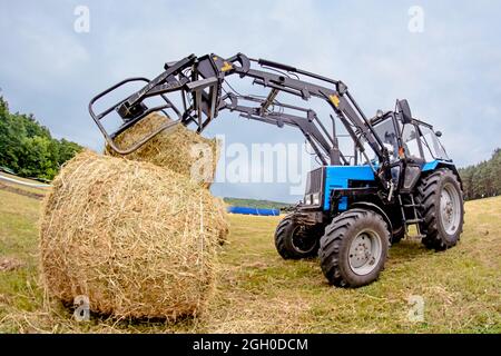 Cherkasy, Ucraina - 16 giugno 2015: Cataste di fieno del trattore nel campo. Tonalità. Foto Stock