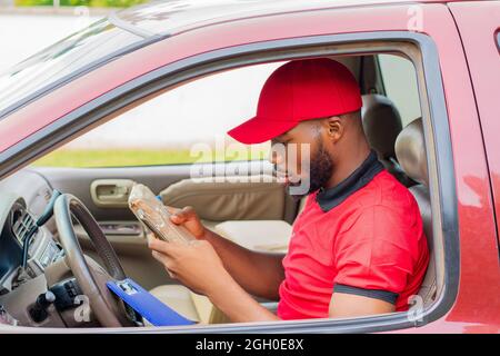 il lavoratore di consegna africano in un'automobile usando il suo telefono Foto Stock