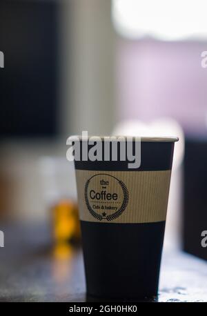 La donna tiene la mano, ha sollevato una tazza di carta kraft di tè o caffè con coperchio. Spazio di copia su sfondo blu. Verticale. Concetto di Foto Stock