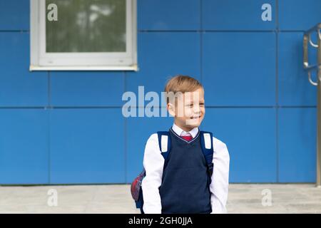 Un ragazzo carino primo grader in una divisa della scuola con una borsa scolastica va a scuola in un giorno d'autunno soleggiato. Celebrazione il 1 settembre. Giornata della conoscenza. Selezionare Foto Stock