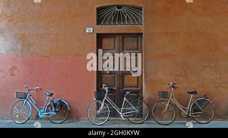 Tre biciclette appoggiate su un muro dipinto di fronte ad una vecchia porta in legno chiusa, a Ravenna, Italia Foto Stock